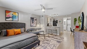 A modern apartment with a large bed, a sofa, a dining area, and a kitchen.