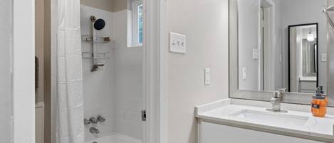 A bathroom with a white bathtub, a shower with a glass door, a large mirror, and a white vanity with a sink.