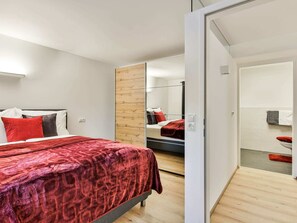 Un dormitorio moderno con una cama, un panel de madera en la pared y un baño visible a través de una puerta abierta.