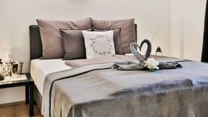 A neatly made bed with a grey blanket and pillows, a decorative swan towel, and a small table with a bottle and glasses. - Inviting Apartment in Inzing With Garden (Inzing)