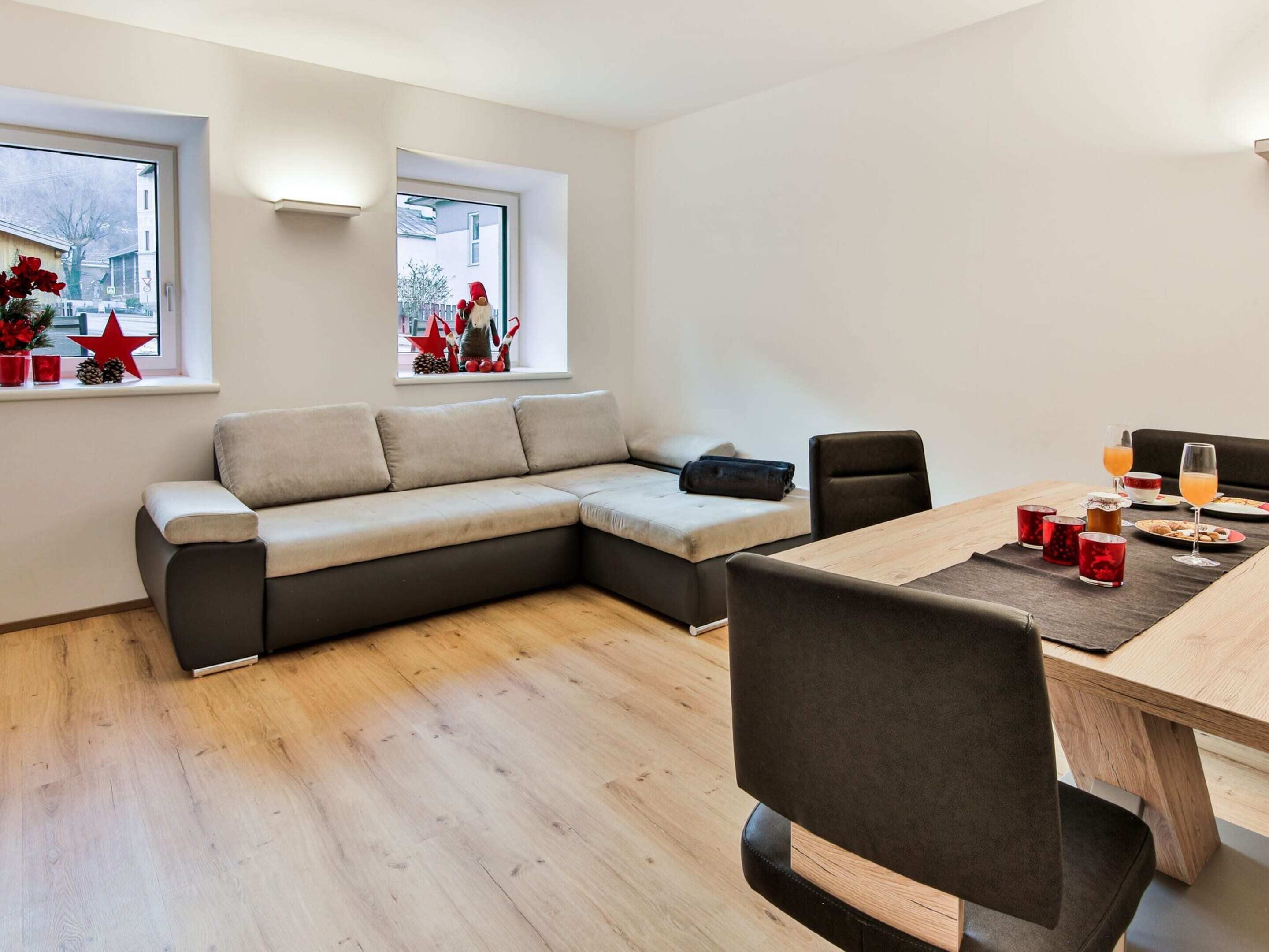 Uma sala de estar moderna com um sofá seccional, uma mesa de jantar e duas janelas com enfeites festivos.