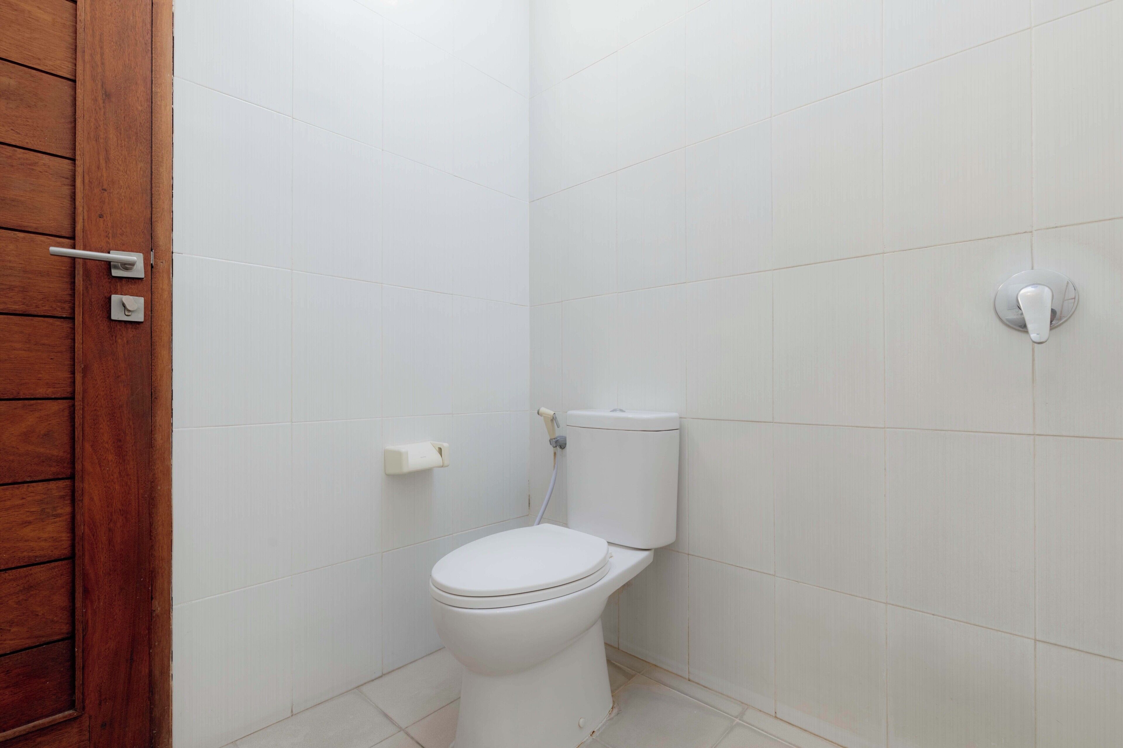 Un baño pequeño y limpio con azulejos blancos, una puerta de madera y un inodoro.