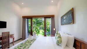Habitación de hotel con cama, escritorio, silla, un cuadro y vista a zonas verdes por la ventana.