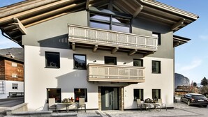 Ein modernes, zweistöckiges Gebäude mit Balkon, Auffahrt und Blick auf die Berge.