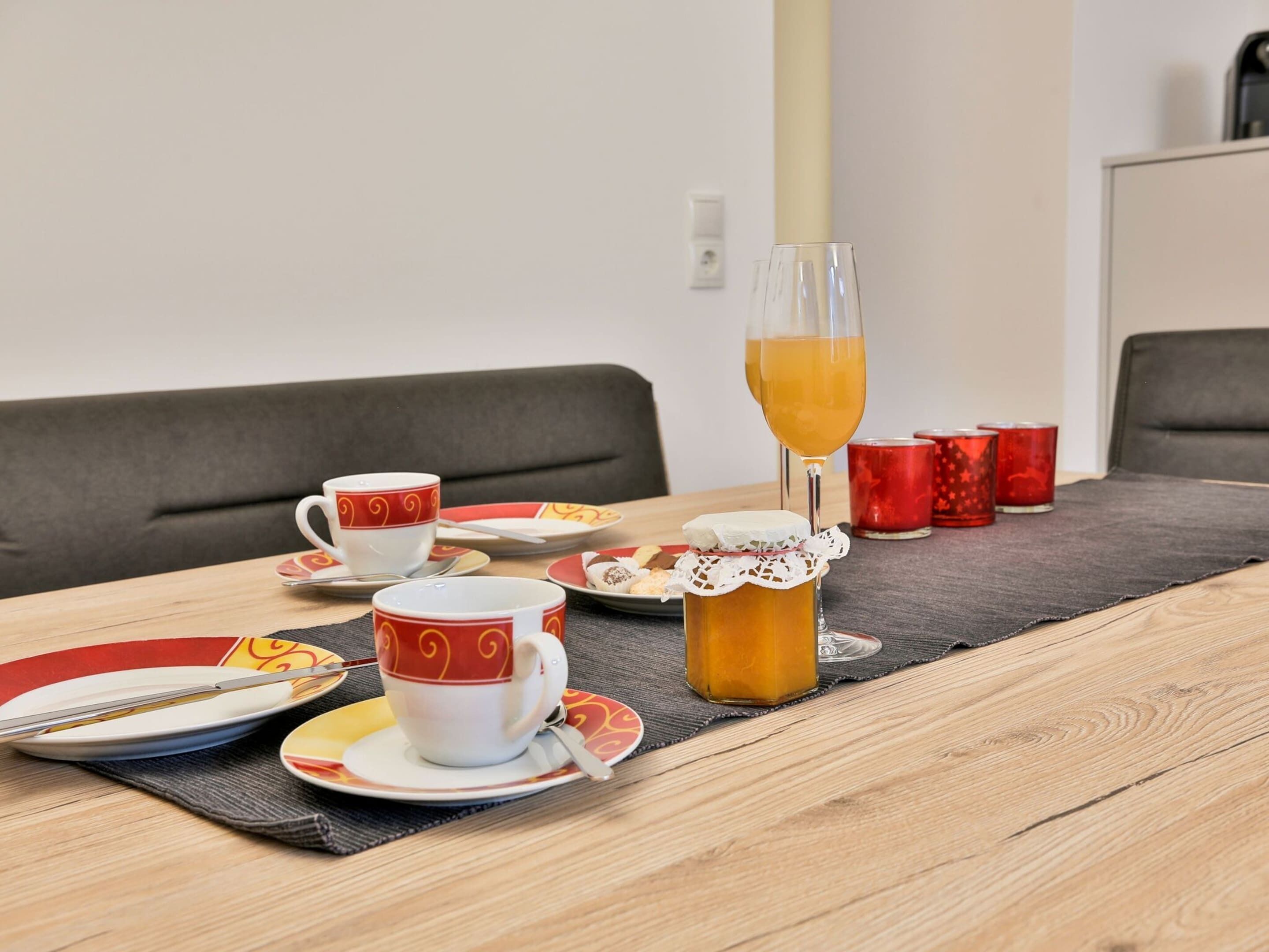 A dining table set with red and white patterned cups, a glass of orange juice, and a pitcher of tea.