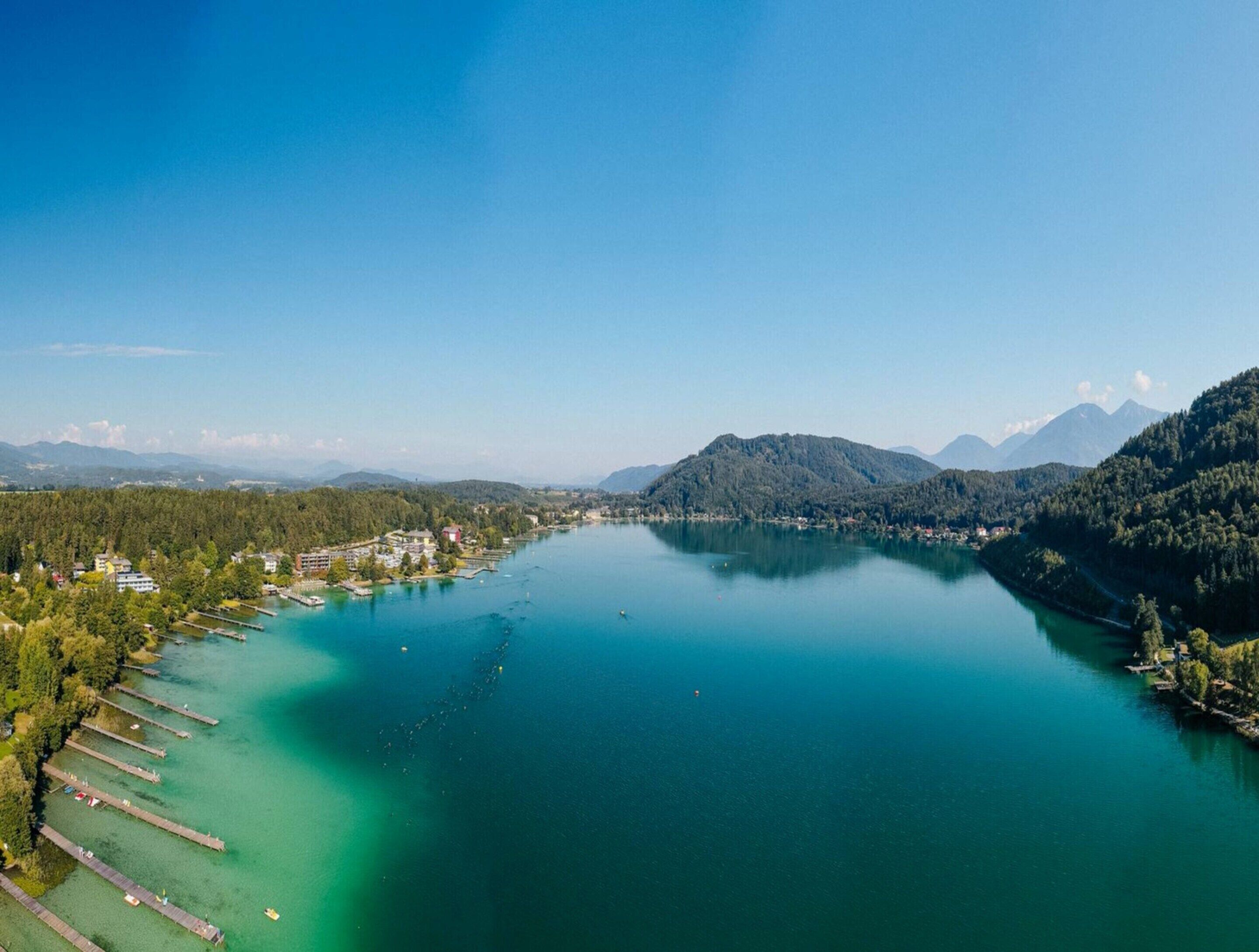 Un lago rodeado de colinas boscosas y un pequeño pueblo con barcos amarrados.