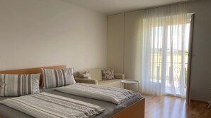 Quarto com uma cama grande, um sofá, uma mesinha e uma janela com cortinas leves.