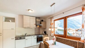 Et køkken med hvide skabe, en komfur og et spiseområde med et bord og stole.