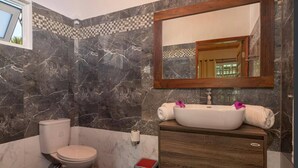 A bathroom with a toilet, sink, mirror, and marble walls.