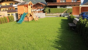 A residential area with a playground, a bench, and a car parked in front of a house with a mountain backdrop.