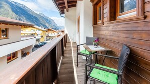 A balcony with wooden railings, a table with a chair, and a view of mountain buildings.