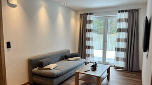Una sala de estar moderna con un sofá gris, una mesa de centro de madera y un ventanal corredizo con cortinas.