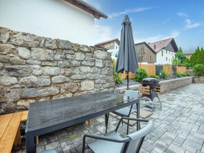 Une terrasse extérieure avec un mur en pierre, une table en bois et un barbecue.