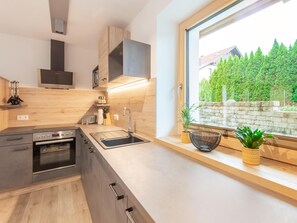 Cocina moderna con horno empotrado, un lavamanos y ventana con vistas a un jardín.