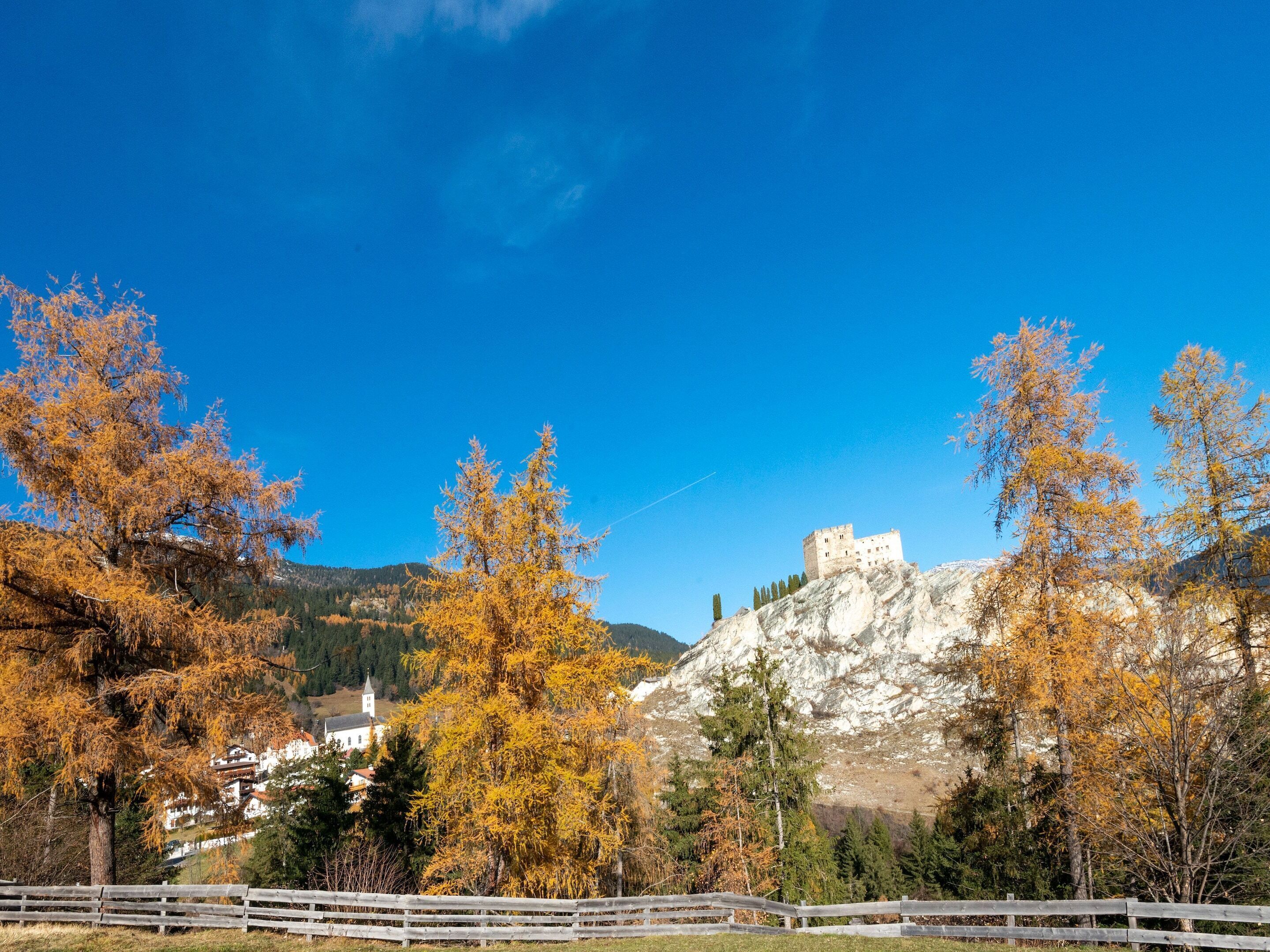 A castle on a hill with autumn trees and a white building in the valley.