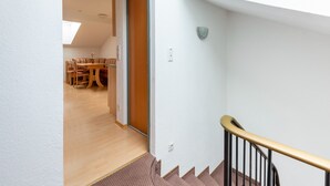A staircase with a wooden handrail leading to a landing. A dining area with a table and chairs is visible in the background. - Cosy Apartment in Ladis With Balcony and View (Ladis)