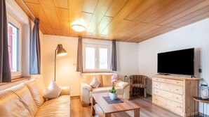 Un salon chaleureux avec un canapé, une table basse en bois, un fauteuil à motifs léopard, un téléviseur et un meuble en bois.