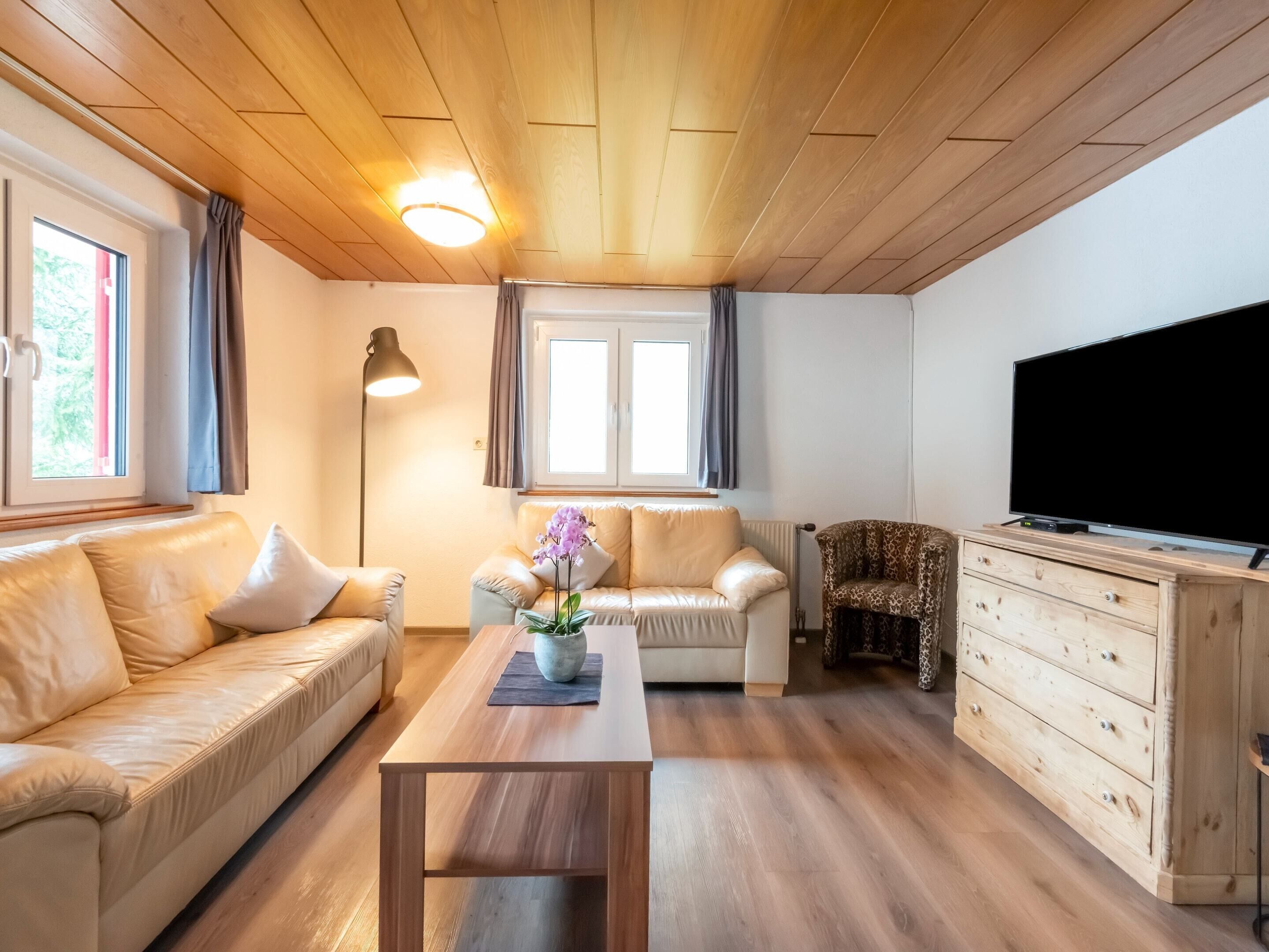 Un accogliente soggiorno con soffitto in legno, un divano, un tavolino, una TV e un mobile.