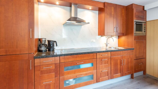 Une cuisine moderne avec des meubles en bois, une hotte en acier inoxydable, un four encastré et un plan de travail en granit.