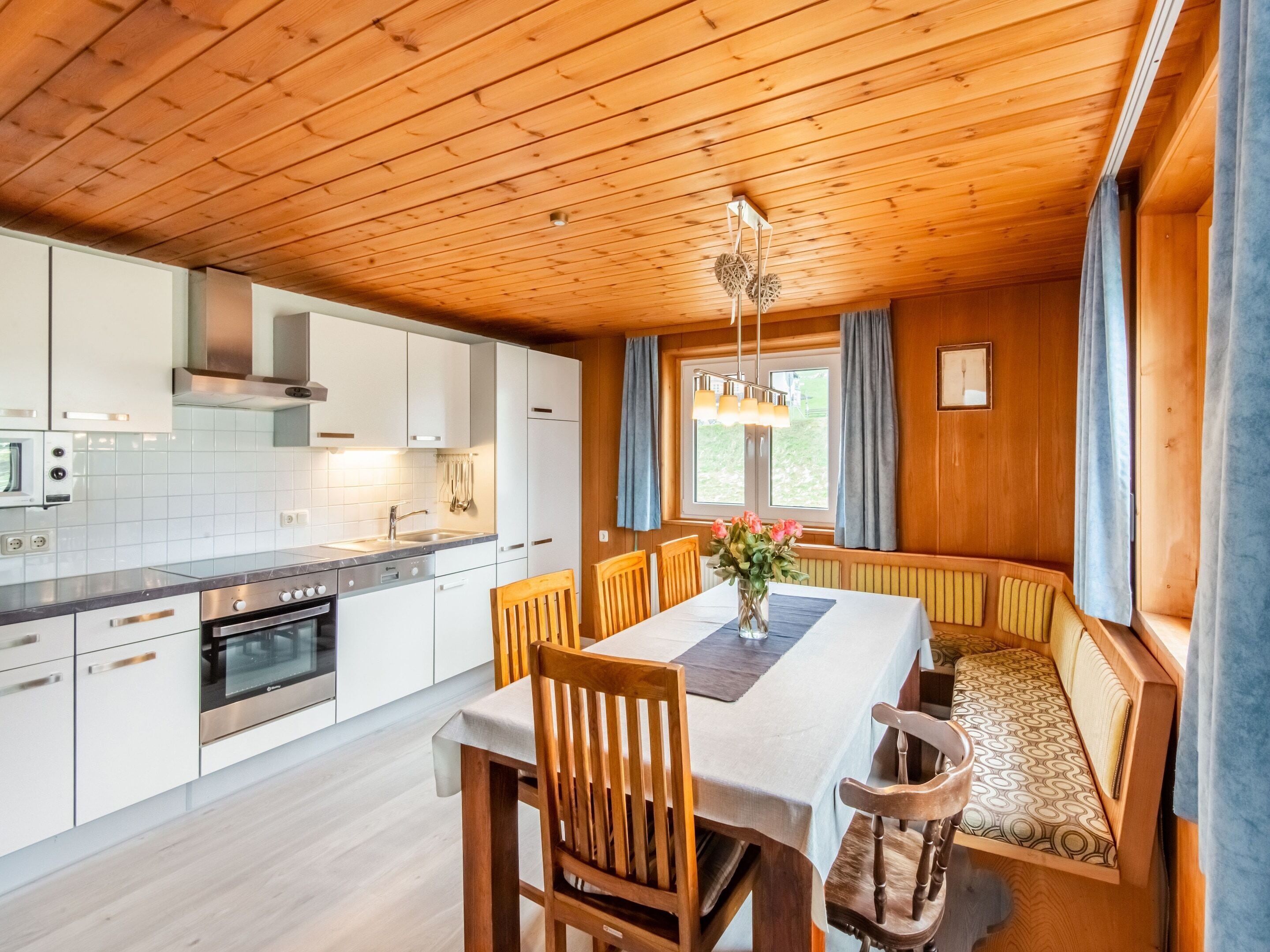 Una cocina moderna con armarios blancos, horno empotrado y zona de comedor con mesa y sillas de madera.