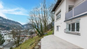 A modern two-story house with a balcony, a stone pathway, and a view of a town and mountains in the background. - Holiday Home Feldkirch Panoramic Views (Feldkirch)