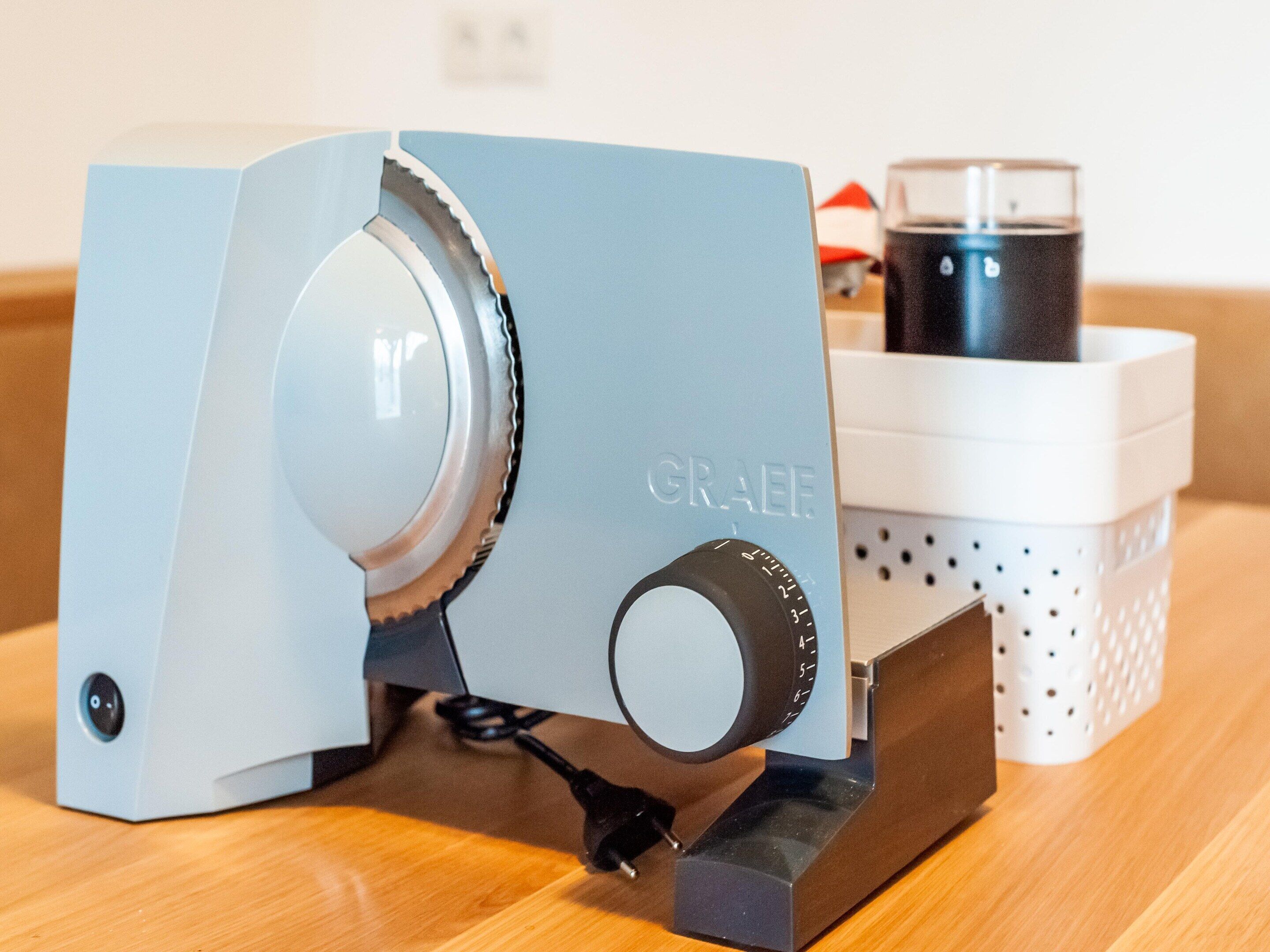A blue and white coffee machine with a control knob, a power cord, and a basket with a coffee cup.