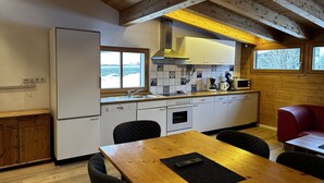 A compact kitchen with a wooden ceiling, a refrigerator, a sink, a stove, and a dining area with a table and chairs. - Apartment in Montafon Near Ski Lifts (Sankt Gallenkirch)