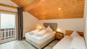 A bedroom with a wooden ceiling, a large window with curtains, a bed with pillows, and a bedside table with a lamp. - Apartment in Montafon Near Ski Lifts (Sankt Gallenkirch)