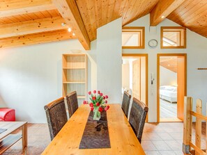 A dining area with a wooden table, wicker chairs, and a vase of red flowers. There is a wooden bookshelf and a door leading to another room. - Apartment in Montafon Near Ski Lifts (Sankt Gallenkirch)