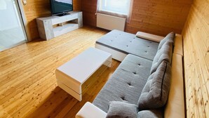 A compact room with a wooden floor, a sofa, a small white table, a television on a stand, and a window with blinds. - Apartment in Salchau Near Lachtal Ski Area (Oberwölz)