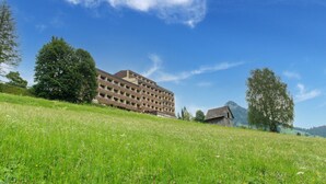 A multi-story building with a flat roof, surrounded by a grassy field and trees. - Apartment Tauplitz Near Ski Lift & Slopes (Bad Mitterndorf)