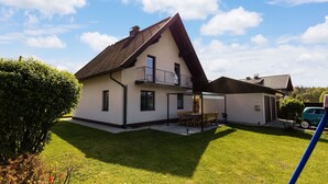 Una casa a due piani con tetto spiovente, un balcone e un piccolo patio con tavolo e sedie.