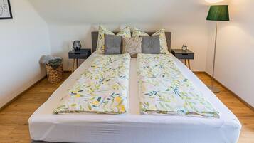 A double bed with a floral bedspread, two nightstands, a floor lamp, and a small basket on the floor.