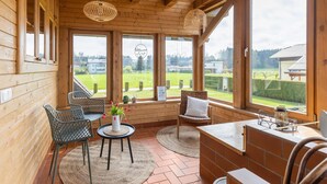 Un interno in legno con ampie finestre, un tavolo rotondo, due sedie e un piccolo tappeto.