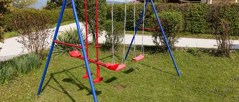 A swing set in a grassy area with a house in the background.
