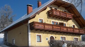 A two-story chalet with a wooden balcony, a sloped roof, and a snow-covered ground. - Apartment in Bleiburg Near the ski Resort (Feistritz ob Bleiburg)