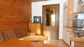 A cozy room with a wooden wall, a sofa, a TV on a cabinet, and a kitchenette with a microwave. - Apartment in Bleiburg Near the ski Resort (Feistritz ob Bleiburg)