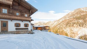 A wooden chalet with a balcony, a stone bench, and a snow-covered landscape with mountains in the background. - Farmhouse in Hochfilzen With Mountain View (Hochfilzen)