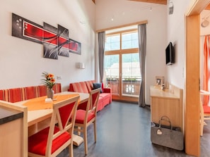 A modern living room with a sofa, dining table, chairs, a TV, and a balcony with curtains. - Well-kept Apartment in a Central Location (Umhausen)