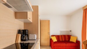 A compact kitchen with a stove, coffee maker, and toaster. A red sofa with yellow pillows is in the living area, and a radiator is visible. - Inviting Holiday Apartment in Ladis With Balcony (Ladis)