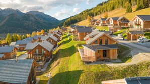 A cluster of wooden cabins with sloped roofs, arranged on a hillside with a view of mountains and a lake. - Chalet in Hohentauern Near Ski Lift (Hohentauern)