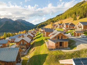 A cluster of wooden cabins with sloped roofs, arranged on a hillside with a view of mountains and a lake. - Chalet in Hohentauern Near Ski Lift (Hohentauern)