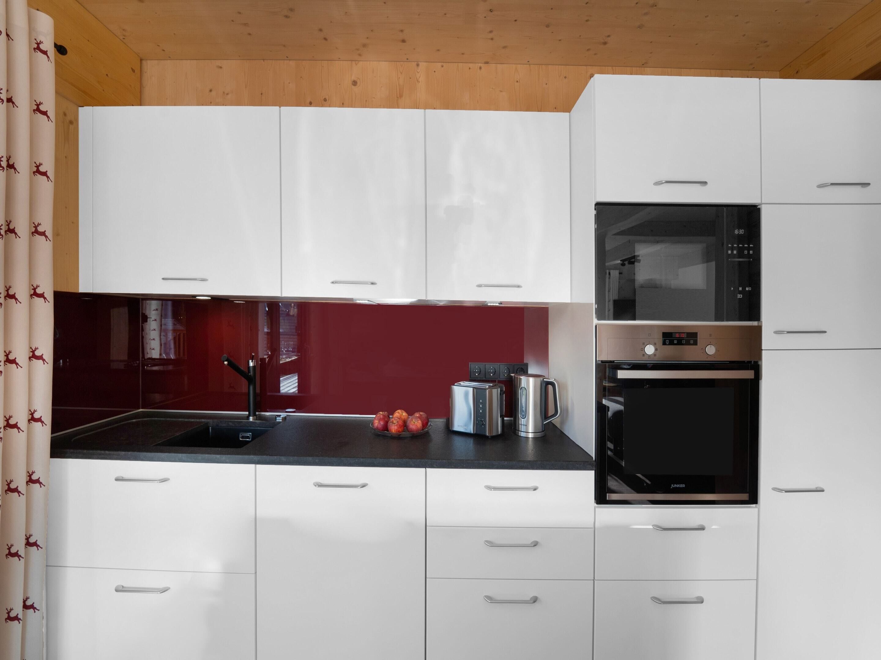 A modern kitchen with white cabinets, a black countertop, a stainless steel kettle, and a built-in oven.