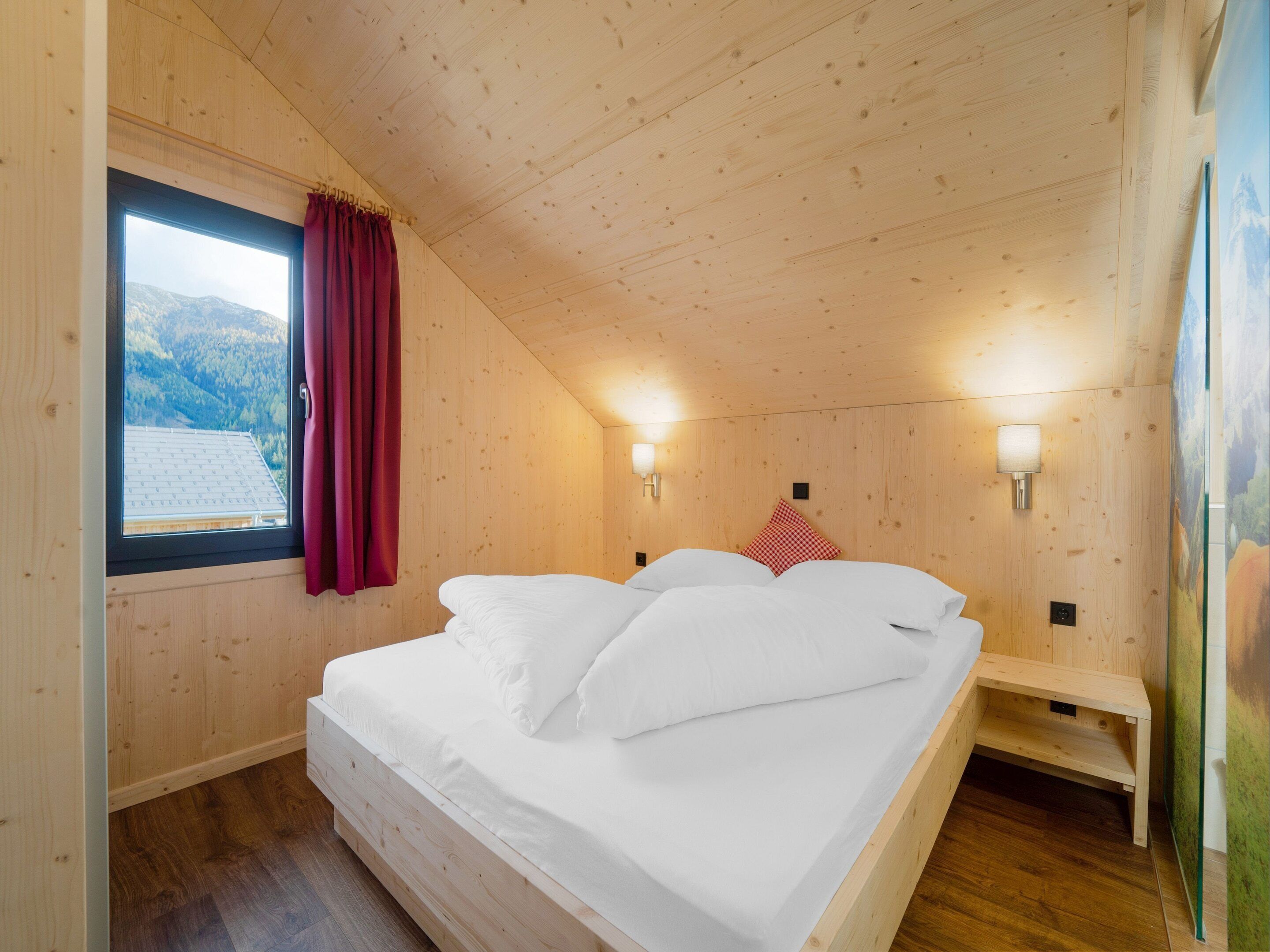 Habitación con paneles de madera, una cama, una ventana con cortinas y dos luces fijadas a la pared.