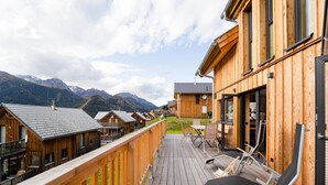 A wooden deck with lounge chairs, a table, and a view of mountains. - Chalet in Hohentauern Near Ski Lift (Hohentauern)