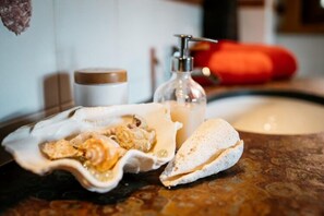 A bathroom counter with a soap dispenser, a jar, and a plate with a pastry.