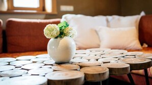Eine weiße Vase mit Blumen auf einem Holztisch mit runden Untersetzern, in einem Raum mit braunem Sofa und weißen Kissen.