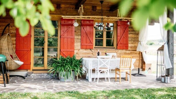 Eine Holzhütte mit einer Steinterrasse, roten Fensterläden und Sitzgelegenheiten im Freien.