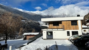 A modern two-story building with a wooden facade and large windows, surrounded by snow-covered mountains and a clear sky. - Apartment in Solden Near Ski Lift (Soelden)
