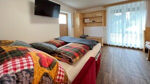 Une chambre à coucher avec un lit, un téléviseur fixé au mur, une armoire en bois et une fenêtre avec des rideaux.